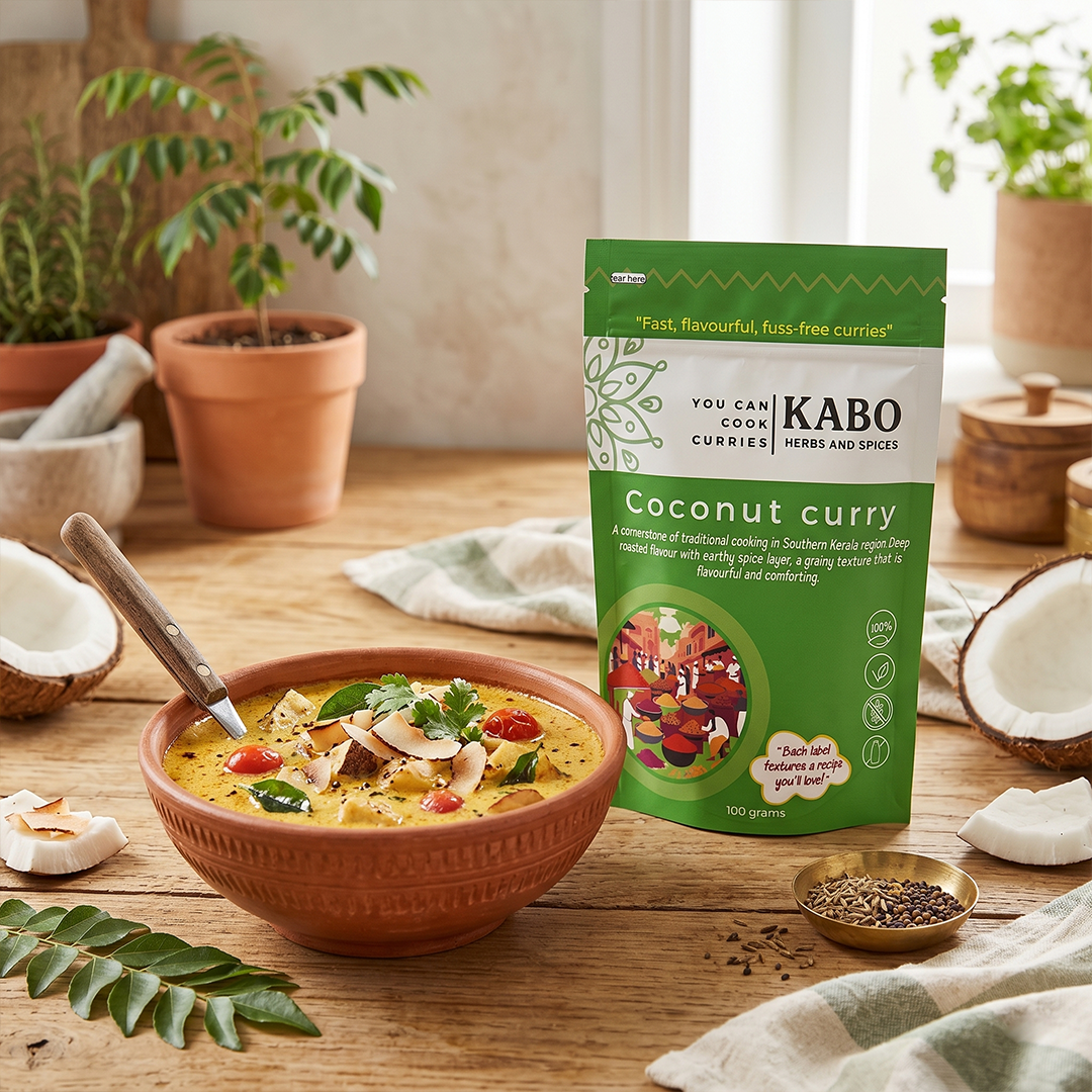 "Kabo coconut curry pouch, mixed vegetabl coconut curry in a mud pot, whole coconut and a curry leaf plant in the background"