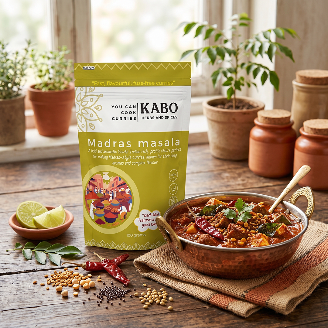 " A pack of Madras curry masala with Madras paneer curry on a kitchen table with lemon slices and curry leaves"